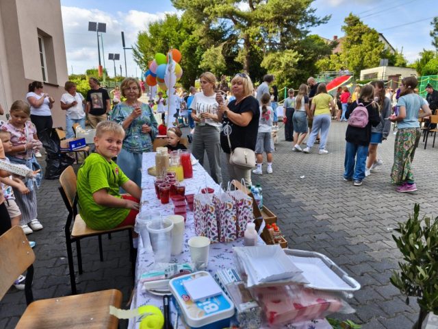 Stoiska z wyrobami ze świeżych owoców na placu szkolnym gdzie odbywa się festyn. Przy stoiskach widać uczniów oraz społeczność lokalną.