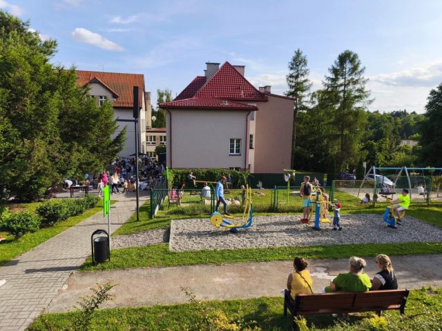 Uczniowie i społeczność lokalna podczas festynu szkolnego. Widok na plac zabaw oraz budynek szkoły