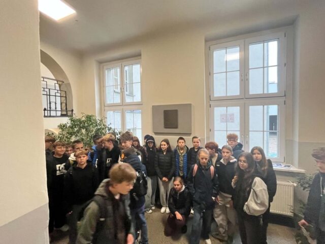 Uczniowie klas 7-mych we wnętrzu budynku przy tablicy pamiątkowej. 